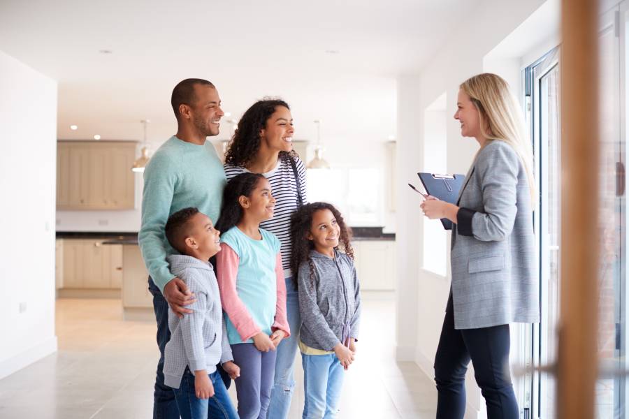 A realtor talking to a family during a home showing. The family includes a mom, a dad, and three children.