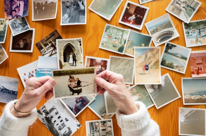A top view of a person looking through printed photographs spread across a table, holding and examining them.