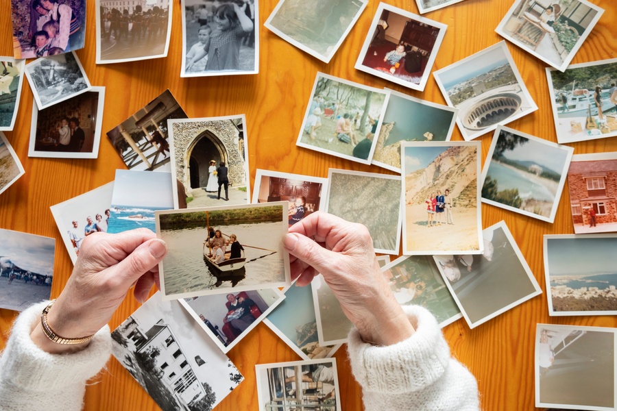 A top view of a person looking through printed photographs spread across a table, holding and examining them.