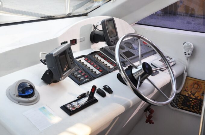 The control board of a boat contains a chartplotter, a steering wheel, and various other switches that control the boat.
