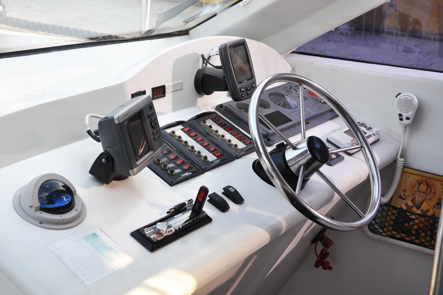The control board of a boat contains a chartplotter, a steering wheel, and various other switches that control the boat.