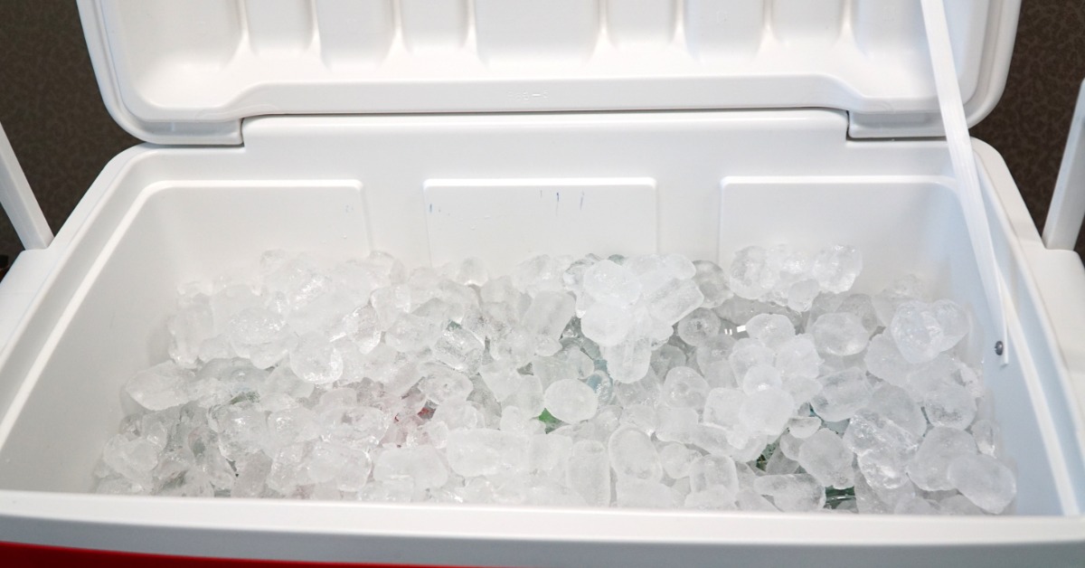 A close-up view shows a red cooler with the white lid open. The inside of the cooler is full of ice.